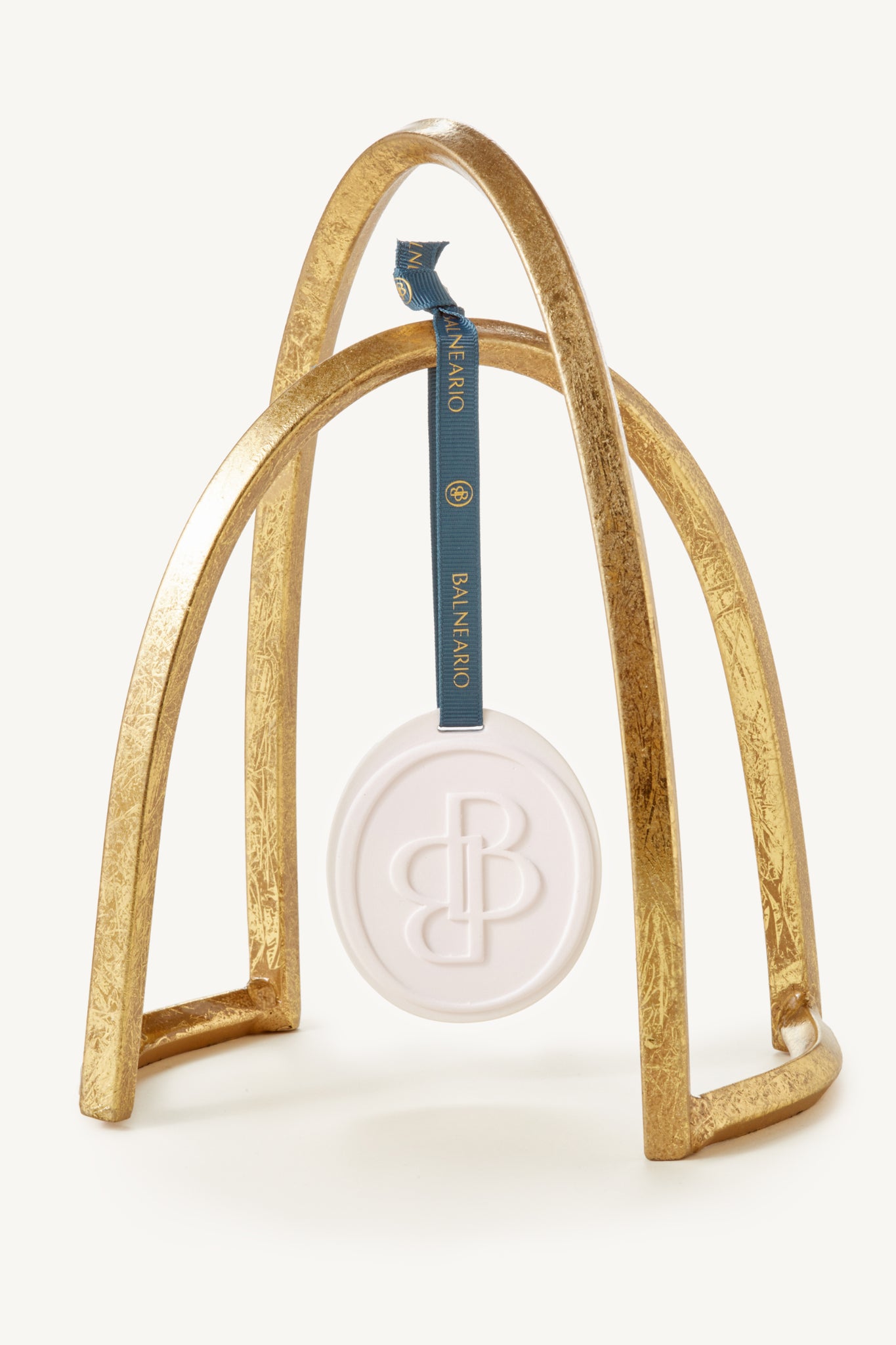 Balneario scented ceramic medallion with signature teal Balneario ribbon hanging from a decorative gold arch