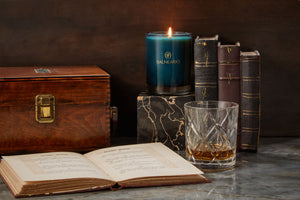 Beautiful image of Balneario candle in a library next to old books and whisky glass.