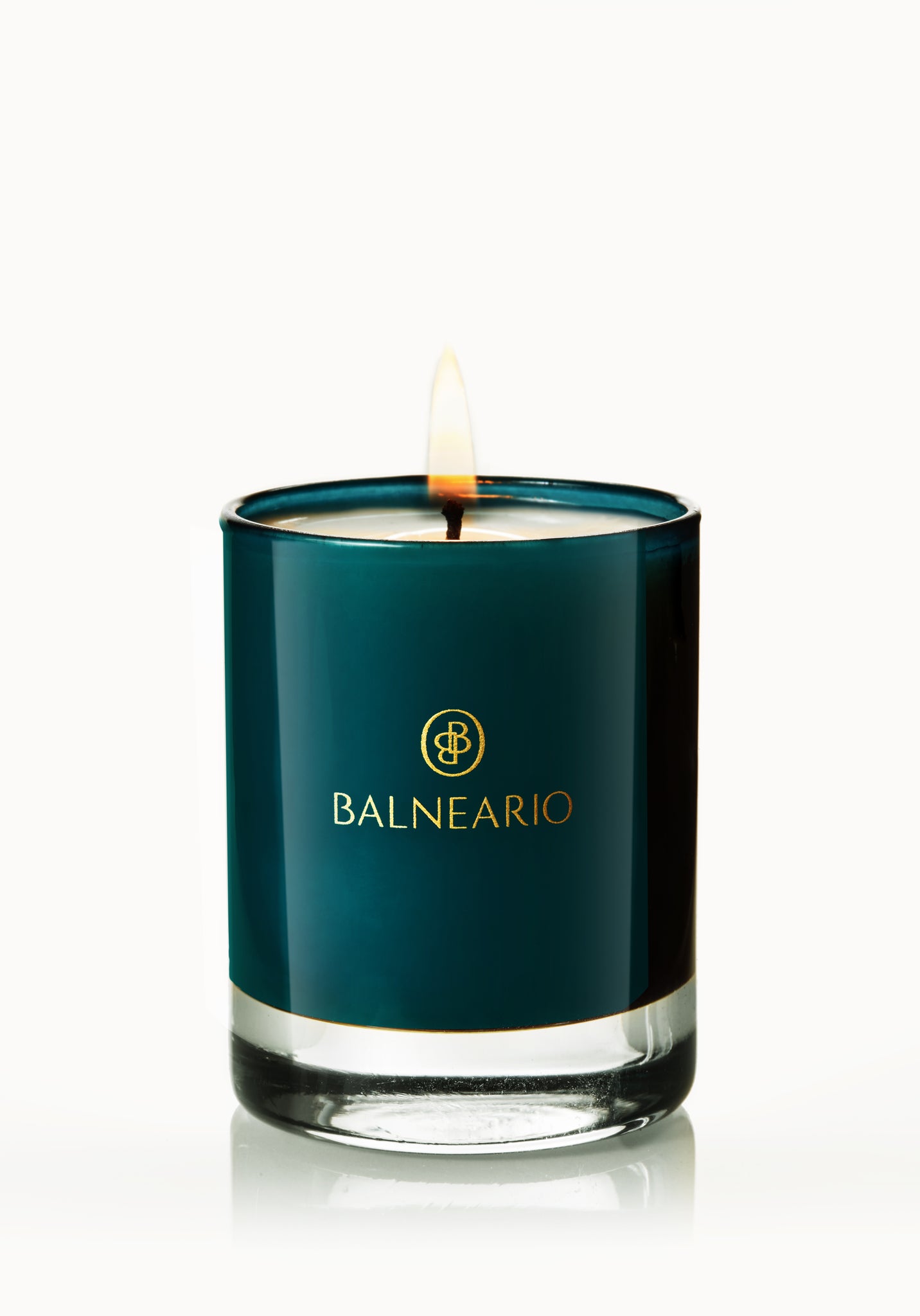 Single 2.5oz Balneario Luxury Soy-Coconut Votive Candle in teal glassware, with a flame.