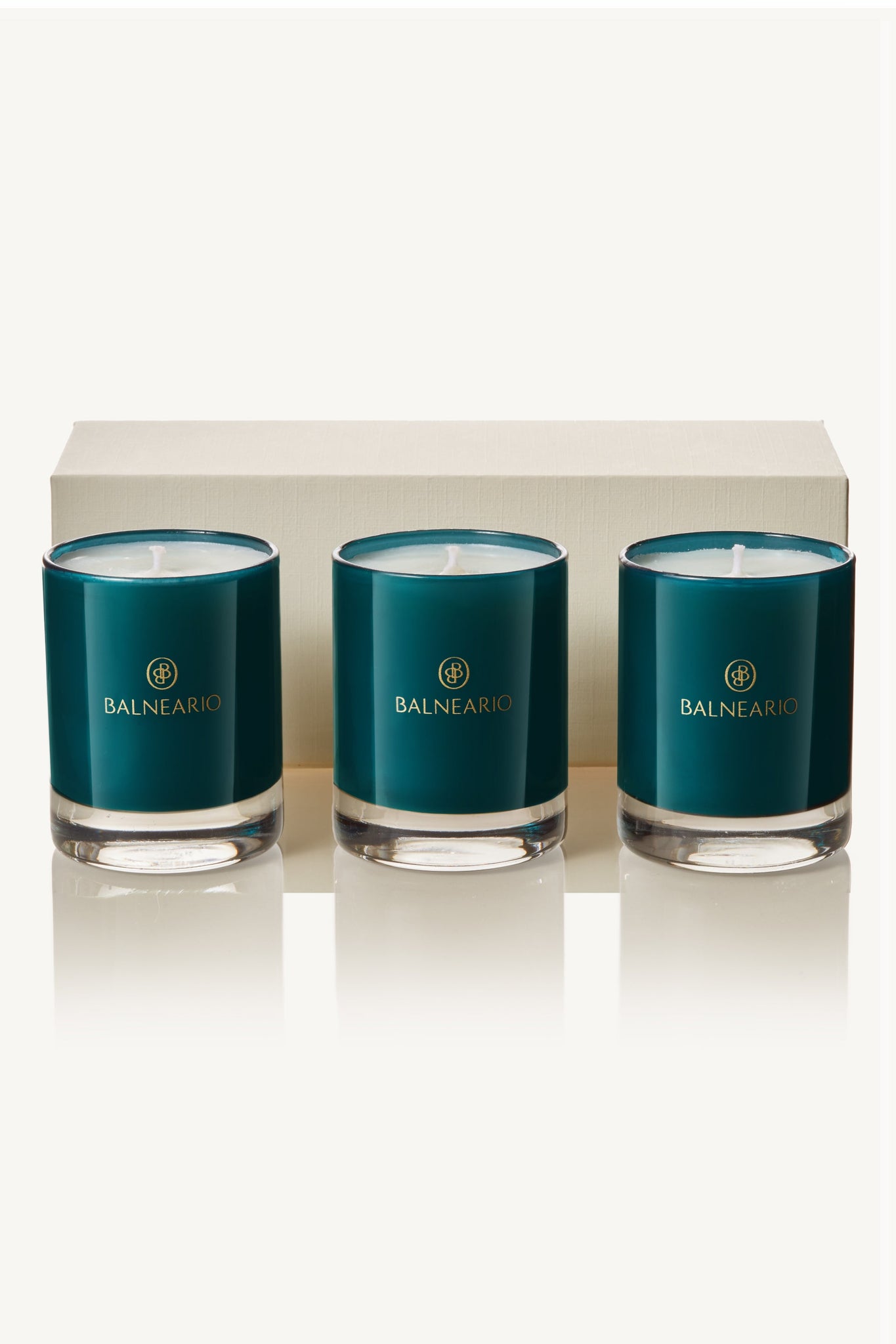 Balneario Luxury Soy-Coconut Votive Candle Trio showcased in signature ocean-hue teal glassware, positioned in front of a gift box.