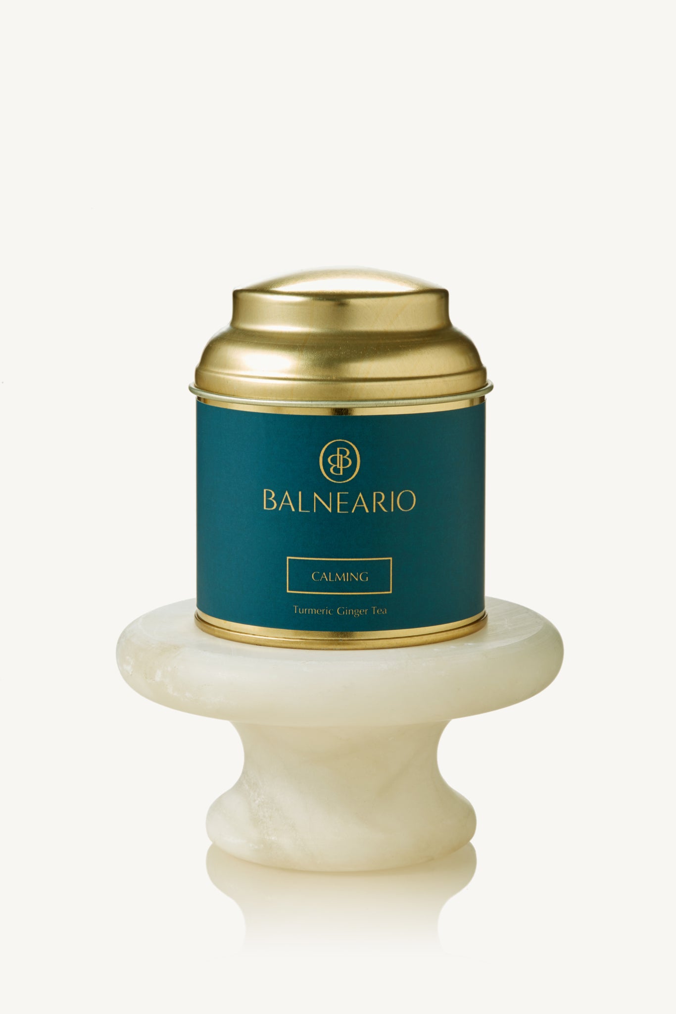 Balneario Calming Wellness Tea in a teal tin with a gold lid, displayed on a small marble pedestal 