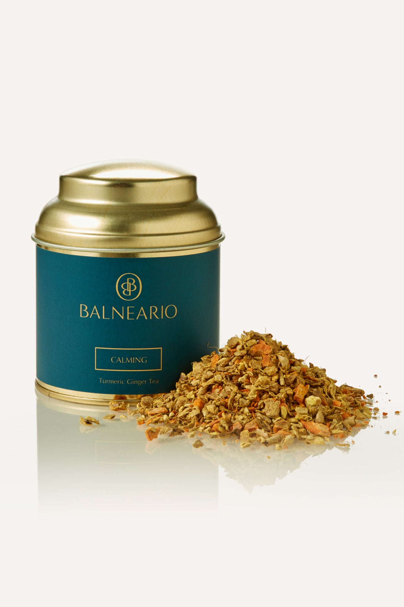 Balneario Calming Wellness Tea in a teal tin with a gold lid, alongside a fragrant pile of calming loose tea leaves.  