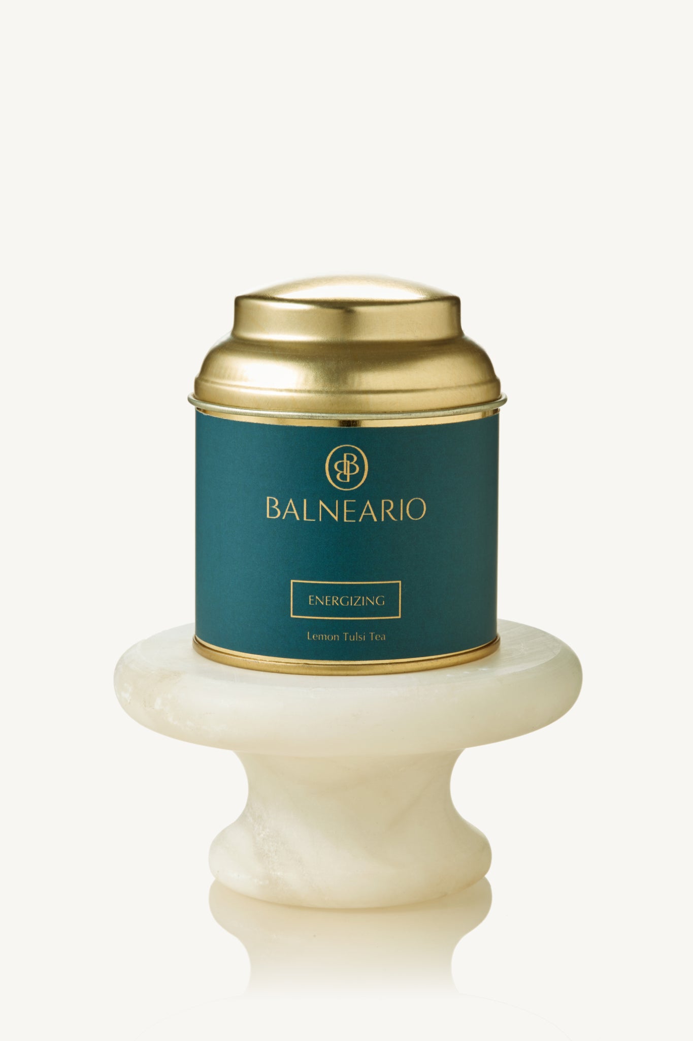 Balneario Energizing Wellness Tea in a teal tin with a gold lid, displayed on a small marble pedestal 