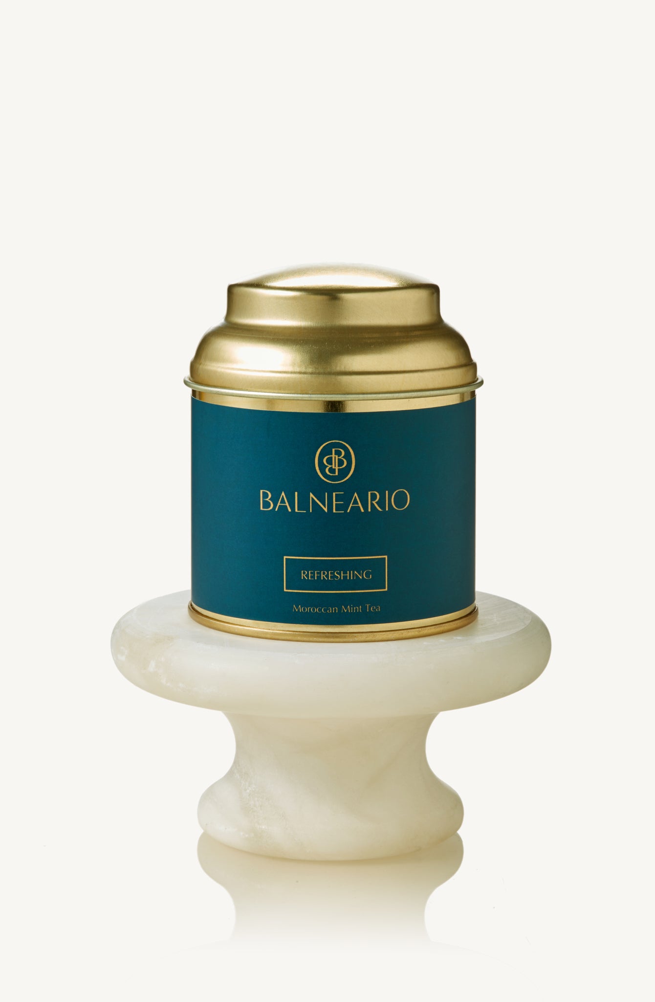 Balneario Refreshing Wellness Tea in a teal tin with a gold lid, displayed on a small marble pedestal 