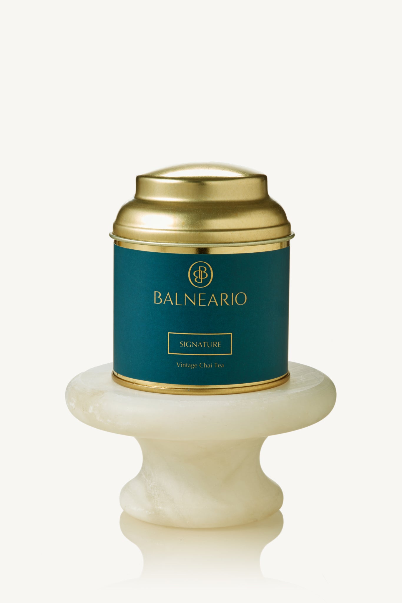 Balneario Signature Wellness Tea in a teal tin with a gold lid, displayed on a small marble pedestal 