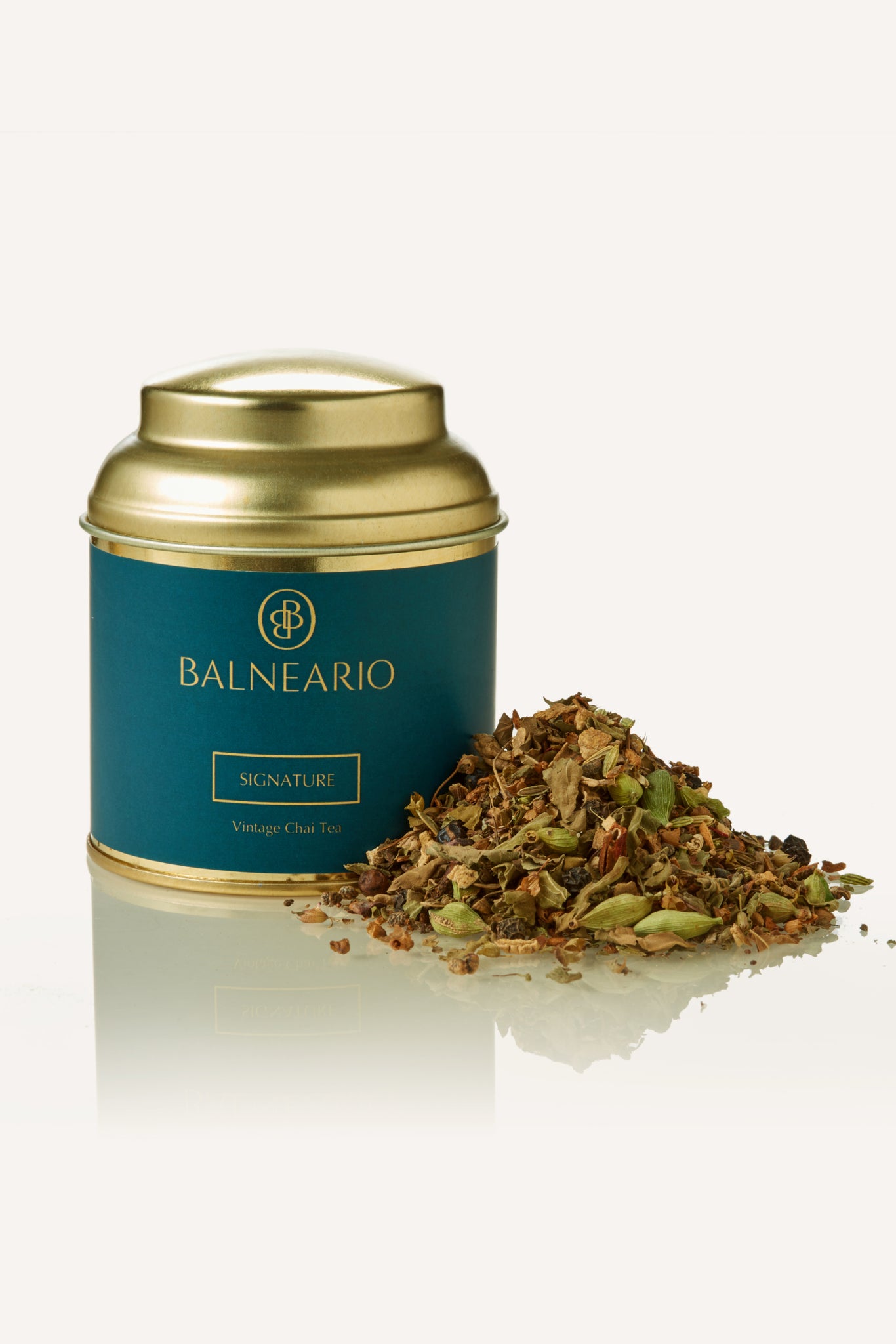 Balneario Signature Wellness Tea in a teal tin with a gold lid, alongside a fragrant pile of loose signature chai tea leaves.