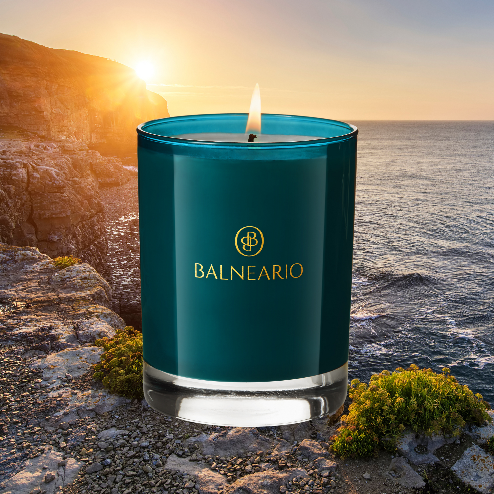 Single Balneario 10.5 oz Luxury Soy-Coconut Candle in teal glassware artfully arranged in front of a beach sunset to represent the Coastal fragrance